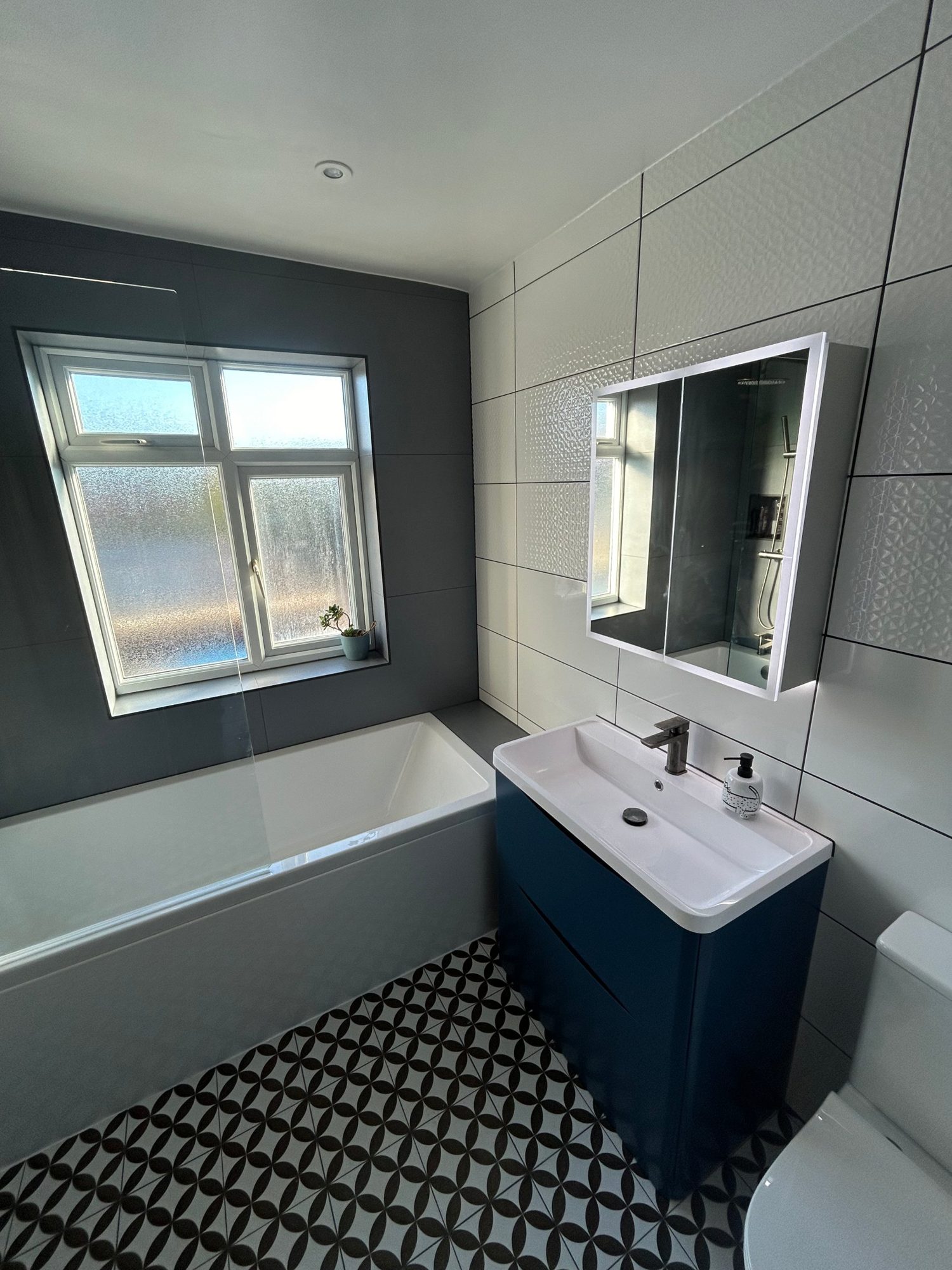 Bathroom with blue vanity, bath and patterned floor tiles by Camms Bathrooms