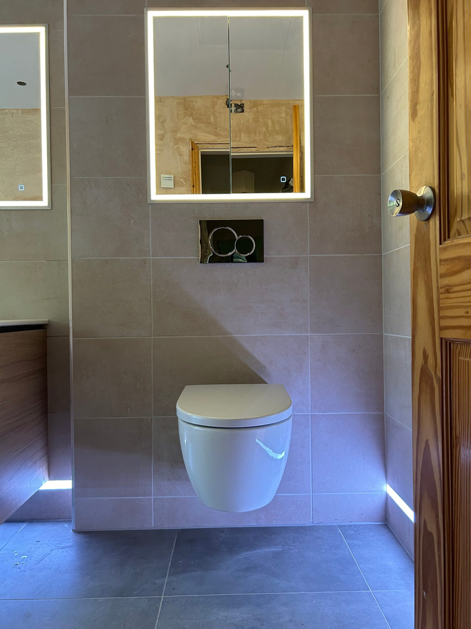 Wall-hung toilet with concealed cistern, LED mirror cabinet and plinth lighting fitted by Camms Bathrooms