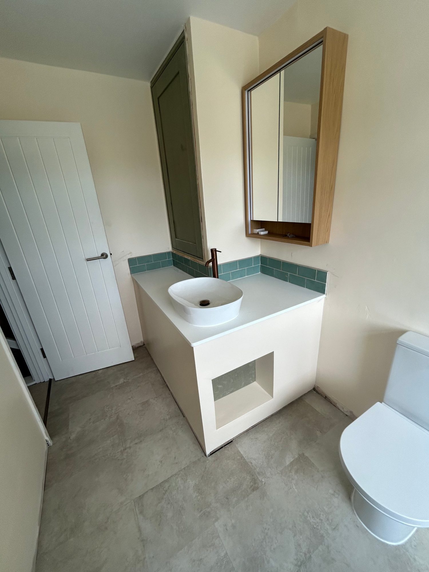 Bathroom with vessel basin, wood-framed mirror cabinet and green tiles