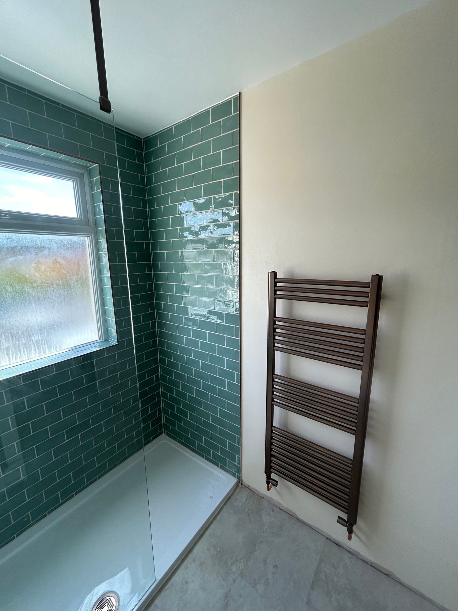 Walk-in shower with green metro tiles and bronze towel radiator