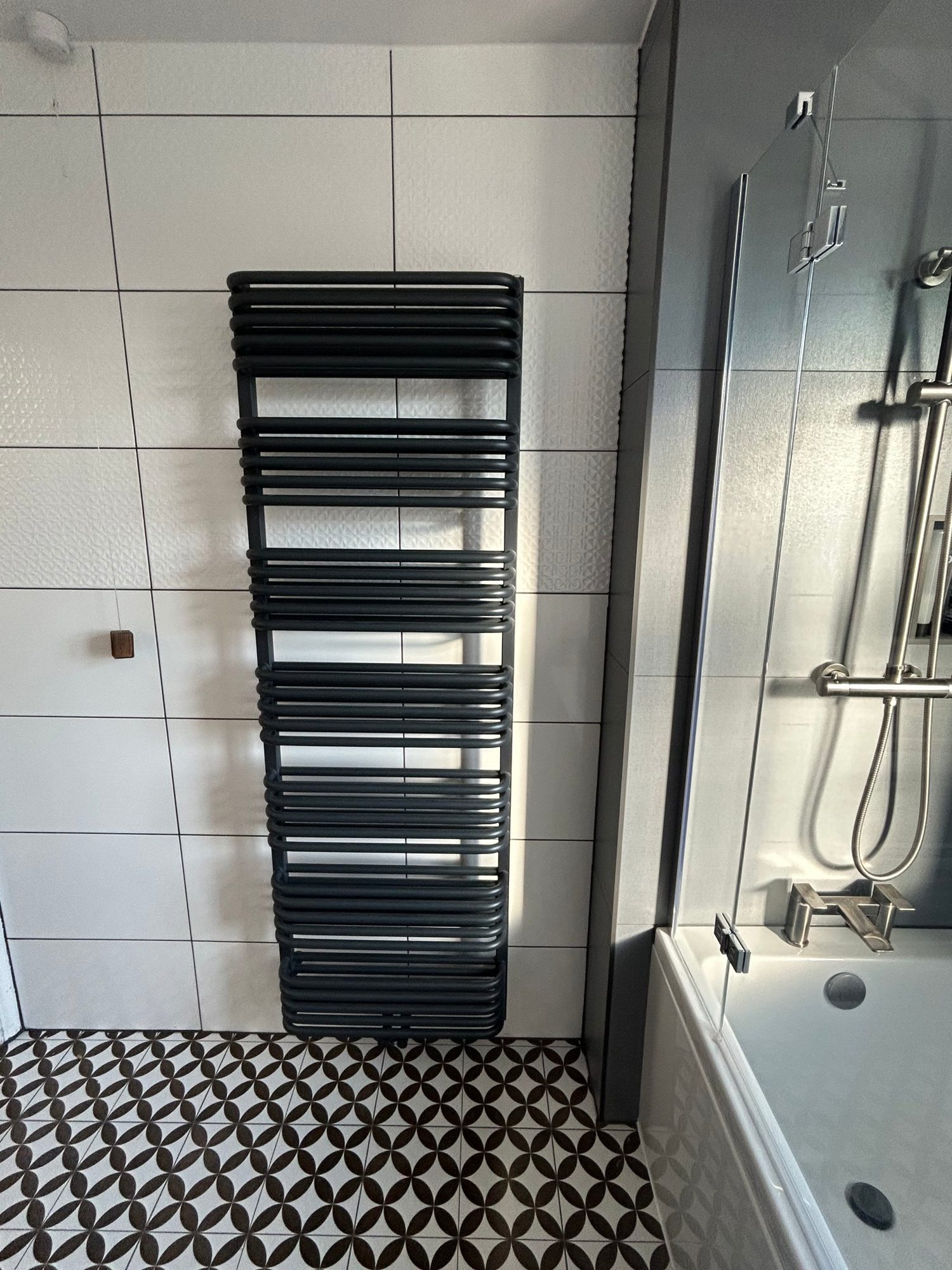 Anthracite towel radiator beside a bath with patterned floor